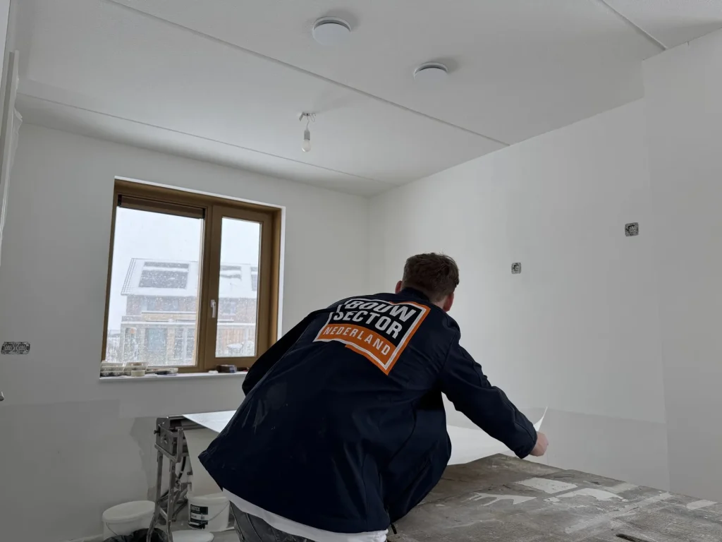 Behanger van Bouwsector Nederland in donkerblauwe jas legt een baan op de plaktafel in een nieuwbouwkamer