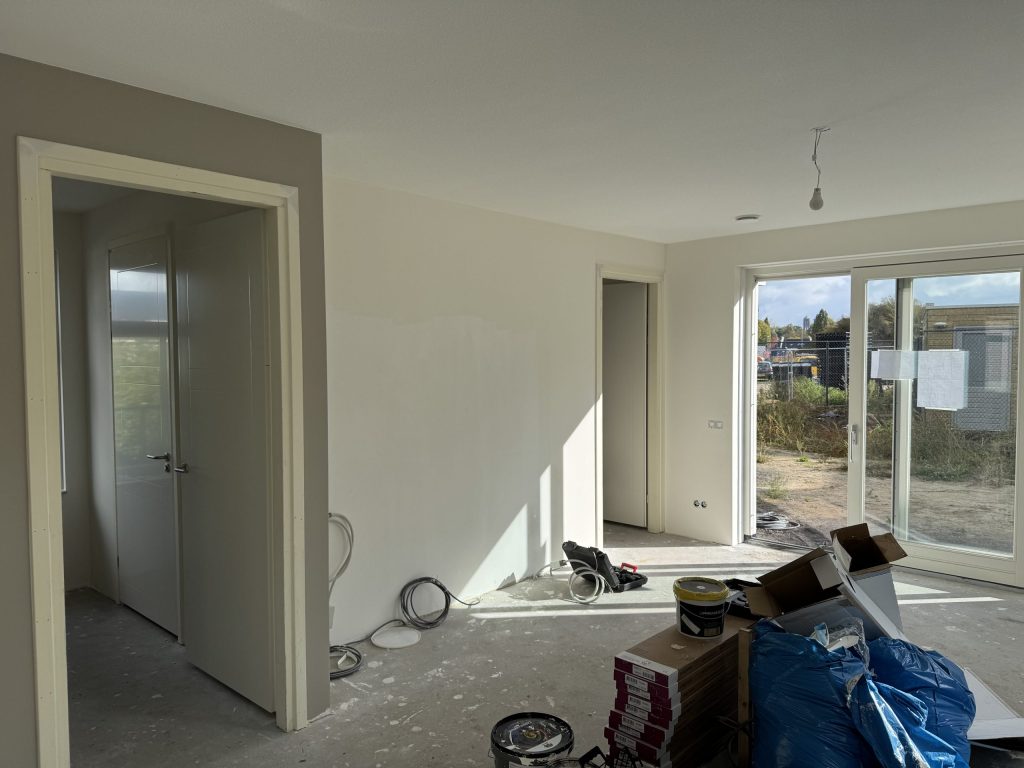 Nieuwbouwwoning tijdens de afwerking met gladde wanden, materiaal op de vloer en een schuifpui naar de tuin