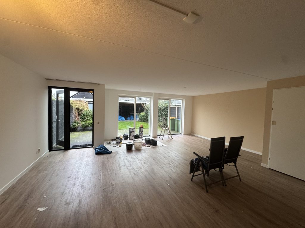 Lege woonkamer met lichte wanden, een laminaatvloer, verfemmers en tuindeuren